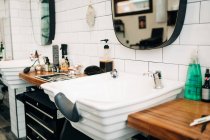 Table avec assortiment de produits cosmétiques en bouteilles et distributeurs entre lavabos sous miroirs réfléchissant salon de coiffure — Photo de stock