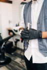 Cropped unrecognizable adult bearded male hairstylist in waistcoat standing in barbershop holding tools — Foto stock