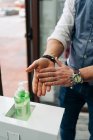 Crop anonymous male barber in wristwatch applying antibacterial gel on hands at work in beauty salon — Stock Photo