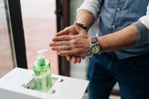 Crop anonymous male barber in wristwatch applying antibacterial gel on hands at work in beauty salon — Stock Photo