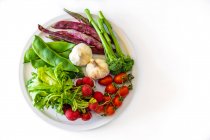 Top view of fresh green beans garlic cherry tomatoes on branch with radish and greens on plate above white background — Stock Photo