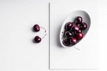 Високий кут здорових стиглих смачних вишень у керамічній мисці, розміщеній на білій дошці — стокове фото