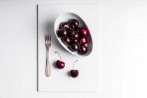 Alto ângulo de saudável cerejas maduras saborosas em tigela de cerâmica colocada no tabuleiro branco — Fotografia de Stock