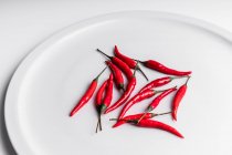 High angle composition of hot red chili peppers arranged around plate against white background — Stock Photo