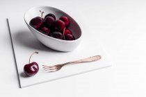 Hohe Winkel der gesunden reifen schmackhaften Kirschen in Keramikschale auf weißem Brett platziert — Stockfoto