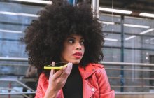 Vue latérale de heureuse femme afro-américaine avec les cheveux bouclés souriant largement tout en parlant sur smartphone sur la rue de la ville — Photo de stock