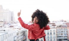 Back view of African American female with curly hair in stylish outfit standing on balcony and looking at city buildings — Stock Photo
