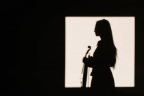 Silueta vista lateral violinista femenina de pie con instrumento musical y cuidadosamente mirando hacia otro lado - foto de stock