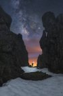 Silueta de explorador anónimo con linterna entre acantilados rocosos y cielo estrellado oscuro en el Parque Nacional Picos de Europa - foto de stock