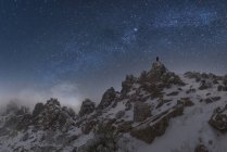 Traveler with glowing flashlight standing on cliff of mountain range in Picos de Europa National Park under dark starry night sky — Stock Photo