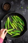 From above crop unrecognizable person holding ripe okra over table with fresh vegetables on frying pan — Stock Photo