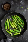 From above ripped fresh okra on frying pan with green pepper on dark background — Stock Photo