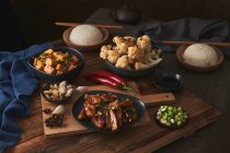 Mala tofu y yuxiang, platos veganos chinos, acompañados de un tazón de arroz, coliflor, salsa de soja y una tetera japonesa encima de una mesa de madera decorada con telas - foto de stock