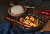 Gros plan tofu mala, plat végétalien chinois, accompagné d'un bol de riz et d'une théière japonaise sur une table en bois décorée de tissus — Photo de stock