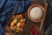 Mala Tofu aus nächster Nähe, chinesisches veganes Gericht, begleitet von einer Schüssel Reis auf einem Holztisch, der mit Stoffen dekoriert ist — Stockfoto