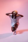Full body of concentrated African American teen dancing with hands outstretched in studio with bright neon light — Stock Photo