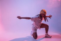 Konzentrierter afroamerikanischer Teenager, der mit ausgestreckten Händen im Studio mit grellem Neonlicht tanzt — Stockfoto