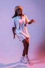 Konzentrierter afroamerikanischer Teenager, der mit ausgestreckten Händen im Studio mit grellem Neonlicht tanzt — Stockfoto