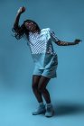 Dynamique afro-américaine adolescente faisant mouvement tout en effectuant la danse urbaine dans la lumière au néon sur fond bleu — Photo de stock