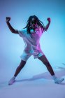 Grave menina adolescente afro-americana em fones de ouvido no pescoço de pé em estúdio com luzes brilhantes de néon — Fotografia de Stock