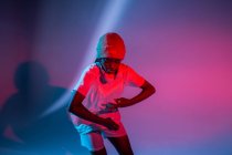 Serious African American teenage girl in headphones on neck dancing in studio with bright glowing neon lights — Stock Photo