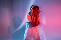African American teenage girl with closed eyes enjoying music in headphones in neon studio — Stock Photo