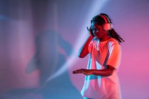 African American teenage girl with closed eyes enjoying music in headphones in neon studio — Stock Photo