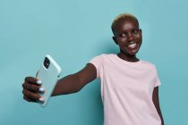 Mulher afro-americana bonita expressiva com manicure brilhante tomando auto retrato no smartphone contra fundo azul — Fotografia de Stock