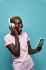 Веселий афроамериканець жіночий зубатий посміхається з закритими очима, слухаючи музику в навушниках на синьому тлі. — стокове фото