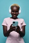 Cheerful African American female toothy smiling while listening to music in headphones against blue background — Foto stock