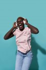 Cheerful African American female toothy smiling looking at camera listening to music in headphones against blue background — Foto stock