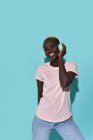 Cheerful African American female toothy smiling looking at camera listening to music in headphones against blue background — Fotografia de Stock