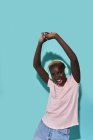 Cheerful African American female toothy smiling with arms raised dancing looking at camera while listening to music in headphones against blue background — Foto stock