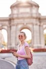 Side view of happy female with backpack browsing mobile phone while exploring Madrid streets — Stock Photo