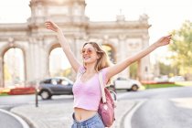 Happy female with hands raised standing in sunshine during trip in Madrid — Fotografia de Stock