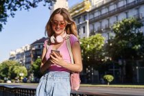 Cheerful woman browsing mobile phone while leaning on handrail on sidewalk on street of Madrid — Stock Photo