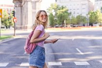 Vue latérale de la jeune femme marchant sur un passage piétonnier et vérifiant l'itinéraire sur un téléphone portable à Madrid — Photo de stock