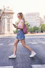 Вид сбоку молодой женщины, идущей по пешеходному переходу и проверяющей маршрут по мобильному телефону в Мадриде — стоковое фото