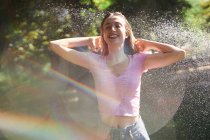 Donna allegra con le mani sulla testa in piedi in spruzzi nel parco soleggiato — Foto stock