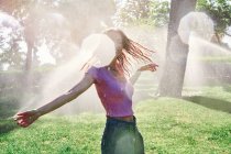 Cheerful female standing in splashes in sunny park — Stock Photo