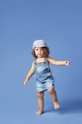 Affascinante bambino scalzo in denim vestito e cappello con i capelli ricci guardando lontano mentre ballava su sfondo blu — Foto stock