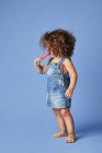 Menina pouco emocional de pé com picolé derretendo contra fundo azul — Fotografia de Stock