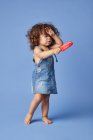 Повне тіло засмученої маленької дівчинки з закритими очима тримає руку на голові, стоячи з морозивом на синьому фоні — стокове фото