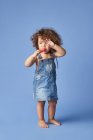 Ganzkörper eines aufgebrachten kleinen Mädchens in Sommerkleidung barfuß stehend mit Eis vor studioblauem Hintergrund — Stockfoto