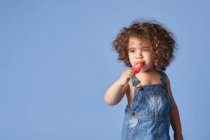Неемоційна маленька дівчинка, що стоїть з таненням віолончелі на синьому фоні — стокове фото