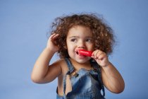 Upset little girl looking away standing with ice cream against studio blue background — Stock Photo