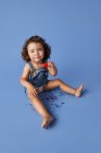 Ganzkörper entzückendes kleines Mädchen, das mit schmelzendem Eis am Stiel vor blauem Hintergrund in die Kamera blickt — Stockfoto