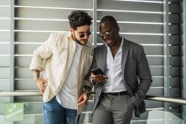 Cheerful multiracial friends looking a cellphone near ribbed wall — Stock Photo