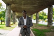 Masculin afro-américain exécutif masculin en costume formel et lunettes de soleil révisant le temps sur la rue — Photo de stock