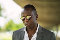 Взрослый афроамериканец-предприниматель в формальной одежде и цепи с серьгой на размытом фоне в солнечном свете — стоковое фото